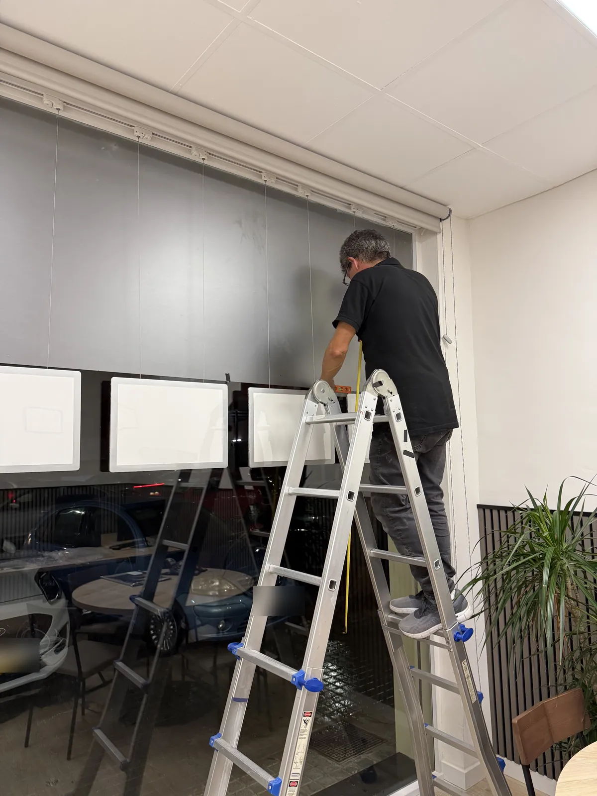 Instalador midiendo y nivelando carpetas LED A3 horizontales colgadas del techo en un ventanal de Catarroja