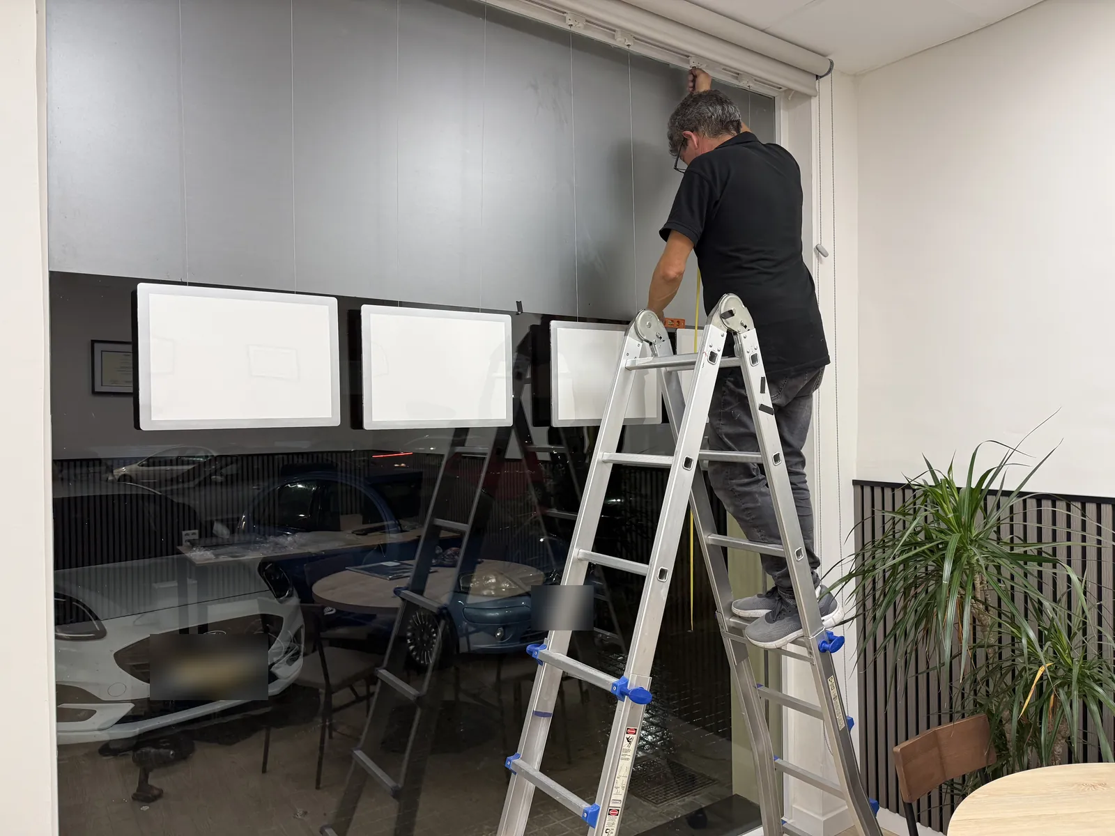Instalador colgando carpetas LED A3 horizontales de un perfil en el techo del ventanal de una inmobiliaria de Catarroja